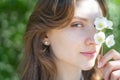 Portrait of a young woman close-up, covering her eye with a branch of jasmine. Beautiful smiling girl with flower in her