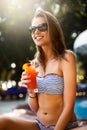 Portrait of young woman with cocktail glass chilling in the tropical sun near swimming pool on a deck chair with palm Royalty Free Stock Photo