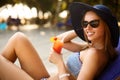 Portrait of young woman with cocktail glass chilling in the tropical sun near swimming pool on a deck chair with palm Royalty Free Stock Photo