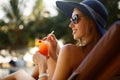 Portrait of young woman with cocktail glass chilling in the tropical sun near swimming pool on a deck chair with palm Royalty Free Stock Photo