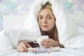 Portrait of young woman with coffee mug and medicines suffering from fever while covered in quilt on bed Royalty Free Stock Photo