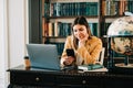 Portrait of young woman college student using mobile phone, preparing for test exam, writing essay doing homework in the library Royalty Free Stock Photo