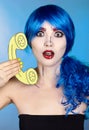 Portrait of young woman in comic  pop art make-up style.  Female in blue wig on blue background calls by phone Royalty Free Stock Photo