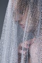 Portrait of a young woman covered with white mesh fabric. A woman hides her face behind a veil cloth