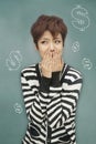 Portrait of young woman covering her mouth in front of blackboard with dollar signs