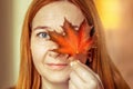 Portrait of a young woman covering one eye with an autumn fallen maple leaf. Autumn mood Royalty Free Stock Photo