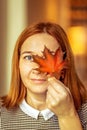 Portrait of a young woman covering one eye with an autumn fallen maple leaf. Autumn mood Royalty Free Stock Photo