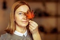 Portrait of a young woman covering one eye with an autumn fallen maple leaf. Autumn mood Royalty Free Stock Photo