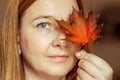 Portrait of a young woman covering one eye with an autumn fallen maple leaf. Autumn mood Royalty Free Stock Photo