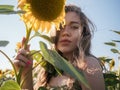 Portrait of young woman covering one eye with sunflower blossom is standing in field of sunflowers, female standing in sunflow at Royalty Free Stock Photo