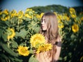 Portrait of young woman covering one eye with sunflower blossom is standing in field of sunflowers, female standing in sunflow at Royalty Free Stock Photo