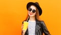 portrait young woman with cup of juice wearing a black round hat, sunglasses over orange background Royalty Free Stock Photo