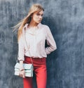 Portrait of a young woman dressed in a blouse, red Chino Trouser, a handbag turquoise on her shoulder. Posing next to a gray wall. Royalty Free Stock Photo