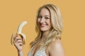 Portrait of a young woman eating banana over colored background