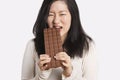 Portrait of a young woman eating a large chocolate bar over light gray background Royalty Free Stock Photo