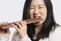 Portrait of a young woman eating a large chocolate bar over light gray background