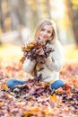 Portrait of a young woman enjoying the autumn atmosphere and playing from maple leaves in park