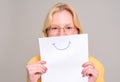 Portrait of young woman in eyeglasses holding white paper with smiley drawing on white background Royalty Free Stock Photo