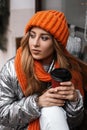 Portrait of a young woman in a fashionable orange hat with a scarf in a winter shiny glamorous jacket near a vintage window.