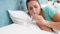 Portrait of young woman feeling unwell lying in bed and dirnking water Royalty Free Stock Photo