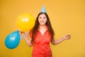 Portrait of a young woman in a festive cap with multi-colored balloons in her hand isolated on a yellow background Royalty Free Stock Photo