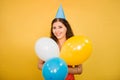 Portrait of a young woman in a festive cap with multi-colored balloons in her hand isolated on a yellow background Royalty Free Stock Photo