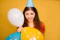 Portrait of a young woman in a festive cap with multi-colored balloons in her hand isolated on a yellow background Royalty Free Stock Photo