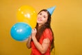 Portrait of a young woman in a festive cap with multi-colored balloons in her hand isolated on a yellow background Royalty Free Stock Photo