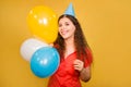 Portrait of a young woman in a festive cap with multi-colored balloons in her hand isolated on a yellow background Royalty Free Stock Photo