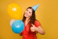 Portrait of a young woman in a festive cap with multi-colored balloons in her hand isolated on a yellow background Royalty Free Stock Photo