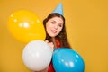 Portrait of a young woman in a festive cap with multi-colored balloons in her hand isolated on a yellow background Royalty Free Stock Photo