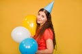 Portrait of a young woman in a festive cap with multi-colored balloons in her hand isolated on a yellow background Royalty Free Stock Photo