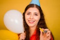 Portrait of a young woman in a festive cap with multi-colored balloons in her hand isolated on a yellow background Royalty Free Stock Photo