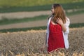 Portrait of young woman in field of wheat. Girl wears red polka dot dress and white shirt looks away Royalty Free Stock Photo