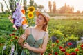 Portrait of young woman gardener holding bunch of fresh gladiolus in summer garden. Farmer picked bouquet of flowers