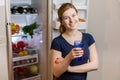 Portrait of a young woman with glass of water in front of the refrigerator full of food