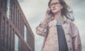 Portrait of young woman in glasses standing outdoors and talking on cellphone.Girl is walking along city street Royalty Free Stock Photo