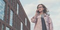 Portrait of young woman in glasses standing outdoors and talking on cellphone.Girl is walking along city street Royalty Free Stock Photo