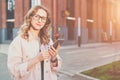 Portrait of young woman in glasses standing outdoors and using smartphone. Royalty Free Stock Photo