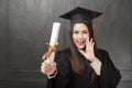 Portrait of young woman in graduation gown smiling and cheering on black background