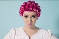 Portrait of young woman grimacing with hair curlers over colored background Royalty Free Stock Photo