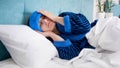Portrait of young woman with headache lying in bed with cold compress on head Royalty Free Stock Photo
