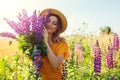 Portrait of young woman holding bouquet of lupin flowers walking in summer meadow. Stylish girl picking blooms