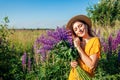 Portrait of young woman holding bouquet of lupin flowers walking in summer meadow. Stylish girl picking blooms Royalty Free Stock Photo