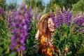 Portrait of young woman holding bouquet of lupin flowers walking in summer meadow. Stylish girl picking blooms Royalty Free Stock Photo