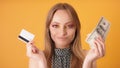 Portrait of a young woman holding cash and credit card. Close up shot isolated on the orange background Royalty Free Stock Photo