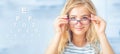 Portrait of young woman holding glasses and looking at camera. Ophthalmological concept with eye test chart Royalty Free Stock Photo