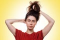 Portrait of a young woman holds her hair in a knot with her hands. Yellow background. Hair care concept