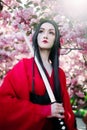 Portrait of young woman in image of geisha with sword in her hand near blooming sakura trees Royalty Free Stock Photo
