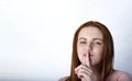 Portrait of young woman keeping finger on her lips and asking to keep quiet, over gray background, Copyspace in left side Royalty Free Stock Photo